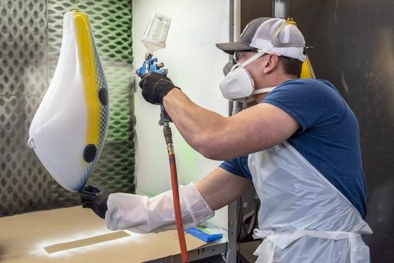 Student sprays a large fishing lure with paint