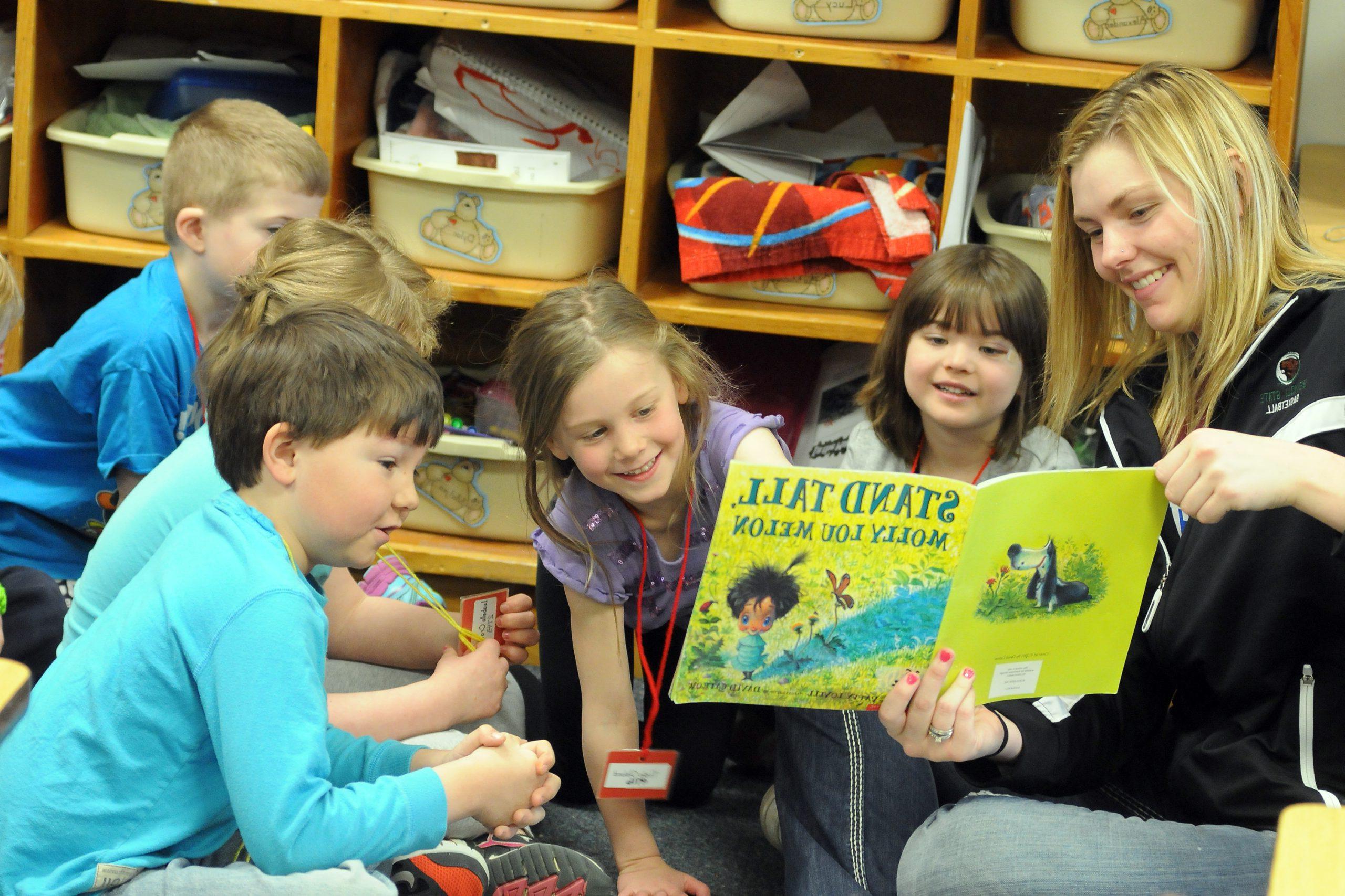 Teacher reading to a group of students from a book called "Stand Tall" by Molly Lou Melon